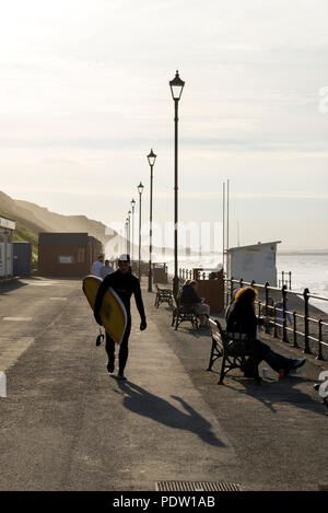 Junge männliche Surfer zu Fuß entlang der Promenade an der Saltburn-by-the-Sea an der Küste von North Yorkshire, England. Stockfoto