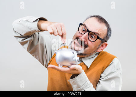 Nerdy Mann ist die Münze in Sparschwein. Stockfoto
