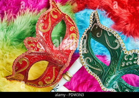 Ansicht von oben, Nahaufnahme die rote und grüne venezianische Maskerade, Karneval Maske (Oper Maske) mit weißem Holz Griff auf die bunten weichen, flauschigen federn, Fanta Stockfoto