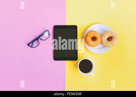 Moderne home office Arbeitsplatz, eine Tasse Kaffee, Donuts, Brillen und Tablet auf gelb rosa Pastell Hintergrund mit Kopie Raum Stockfoto