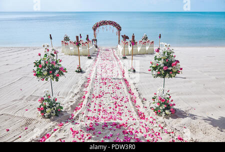 Hochzeit am Strand Veranstaltungsort Einstellung auf dem weißen Sand mit herrlichem Panoramablick auf das Meer im Hintergrund, Rosa und Rote Rosenblätter auf dem Gang Stockfoto