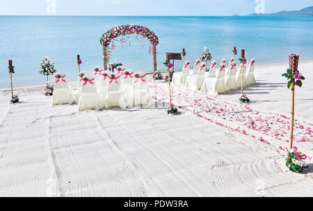 Romantische schöne bunte Hochzeit am Strand mit Panoramablick auf das Meer im Hintergrund, rosa und rote Rosen Blütenblatt am Gang Stockfoto