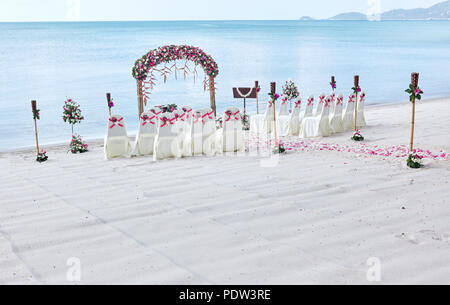 Romantische Hochzeit am Strand Veranstaltungsort Einstellungen am Meer dekorieren mit vielen Rosen Blütenblatt am Gang, blaues Meer Hintergrund Stockfoto