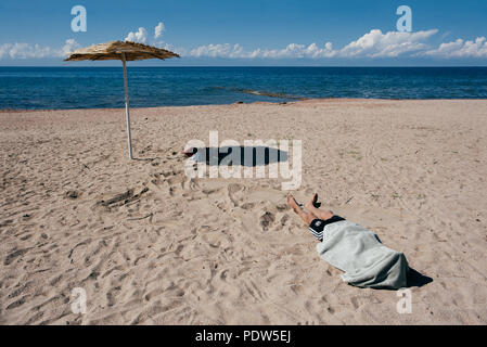Mann schläft an einem Strand mit einem Handtuch auf dem Kopf, See issyk kul in Kirgisistan Stockfoto