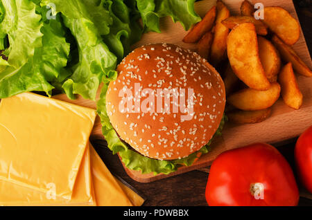 Hausgemachten Zutaten für einen Burger auf einem schwarzen Hintergrund. Käse, Tomaten, Salat und Brötchen auf vintage Holzbretter. Appetitliche Bild über köstliche Stockfoto