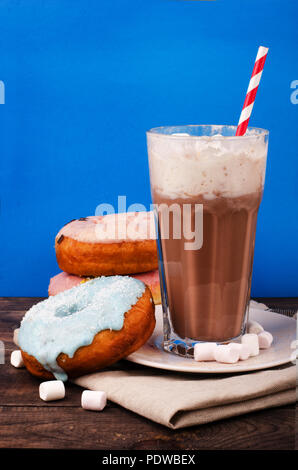 Milchshake und Donuts in Glas auf blauem Hintergrund Stockfoto