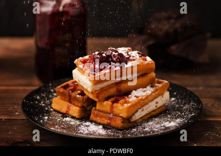 Wiener Waffeln mit Kirsche Konfitüre und Puderzucker auf schwarzem Hintergrund Stockfoto