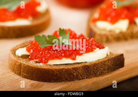 Sandwiches mit imitierter roter Kaviar und Butter auf Holz Schneidebrett auf hölzernen Tisch Stockfoto