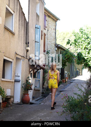 Eine fröhliche und hell gekleidet 16 Jährige blonde Mädchen zu Fuß durch die alten Straßen des Dorfes von Cessenon zu Fuß entfernt von der Kamera Stockfoto