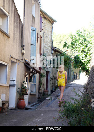Eine fröhliche und hell gekleidet 16 Jährige blonde Mädchen zu Fuß durch die alten Straßen des Dorfes von Cessenon zu Fuß entfernt von der Kamera Stockfoto
