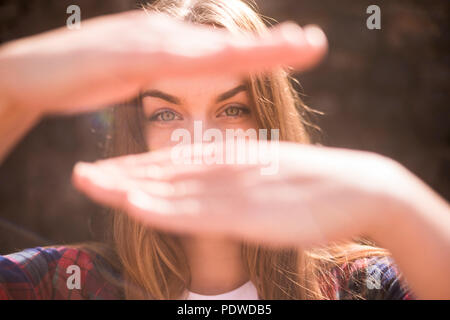 Sonnige Portrait von schönen Modell kaukasischen mit blauen Augen in die Hintergrundbeleuchtung mit der Hand vor ihrem Gesicht die versteckte Mund. bokeh Defokussierten backgroun Stockfoto