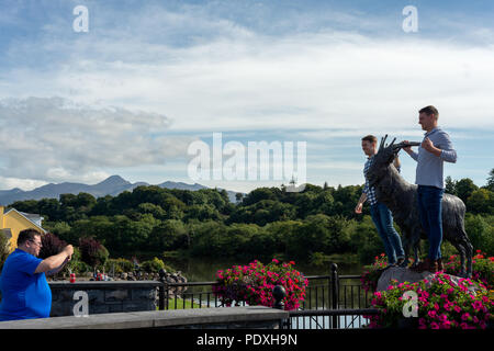 Touristen, die während der Puck Fair - Irlands älteste traditionelle Messe - Spaß haben, während sie Fotos mit der King Puck Statue machen. Irisches Sommerfest. Killorglin, County Kerry, Irland. Stockfoto