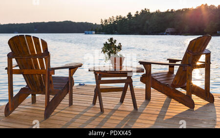 Stühle auf einem Deck mit Blick auf einen See bei Sonnenuntergang. Stockfoto