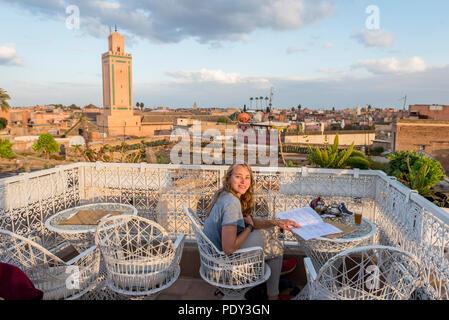 Junge Frau auf einer Dachterrasse liest die Speisekarte im Restaurant, mit Blick auf die Altstadt, Moschee mit Minarett, Abendstimmung Stockfoto