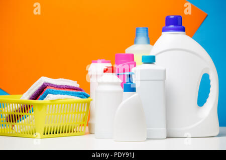 Foto von Flaschen Reinigungsmittel und bunten Bettwäsche in Korb auf blau, orange Hintergrund isoliert, Platz für die Beschriftung Stockfoto