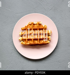Traditionelle belgische Waffel auf rosa Platte über konkrete Oberfläche, Ansicht von oben. Nahaufnahme. Stockfoto