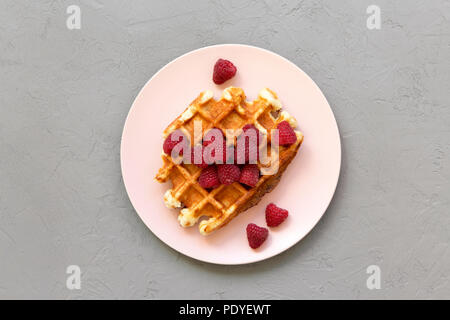 Traditionelle belgische Waffeln mit Himbeeren auf Rosa die Platte über der Betonoberfläche, flach. Von oben und Overhead. Stockfoto