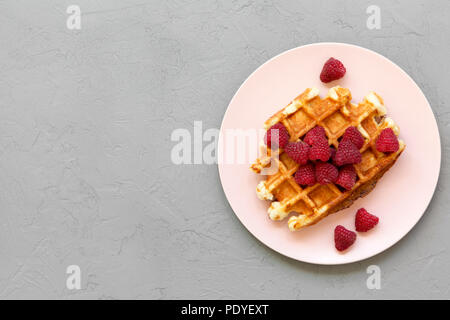 Traditionelle belgische Waffeln mit Himbeeren auf rosa Platte über konkrete Oberfläche, Ansicht von oben. Kopieren Sie Platz. Stockfoto