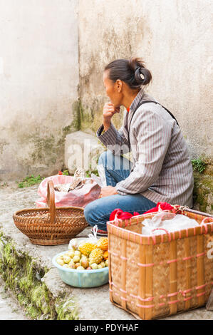 Frau Verkauf von Gemüse, Fleisch und Gewürzen, außerhalb eines kleinen Store angezeigt. Lokale Gerichte und exotische Lebensmittel an einem besetzten Dorf Markt in Asien. Stockfoto