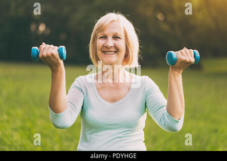 Sportliche ältere Frau Trainieren mit Gewichten outdoor. Bild ist absichtlich abgeschwächt. Stockfoto