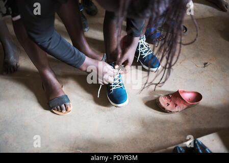 Junge Ugandischen/Afrikanische Schulkinder versuchen auf gebrauchte Schuhe zu der Schule als Geschenk aus dem Vereinigten Königreich gegeben Stockfoto
