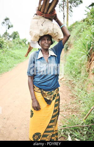 Ugandische Frau, die Bundles aus Holz auf den Kopf in die Kamera lächeln Stockfoto
