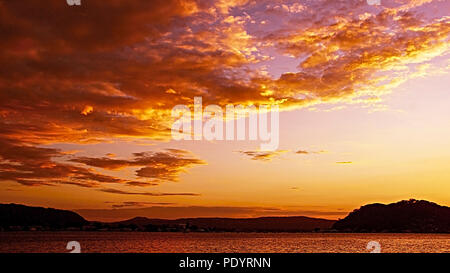 Herrliche Orange skyscape Sonnenuntergang mit vorwiegend Stratocumulus Cloud, in einem Lachs orange gefärbten Himmel. Marine mit Meerwasser Reflexionen. Stockfoto