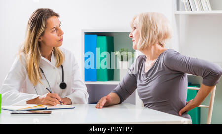 Ältere Patienten erzählen Frauen Arzt, wie Sie mit Schmerzen in ihrem Rücken. Stockfoto