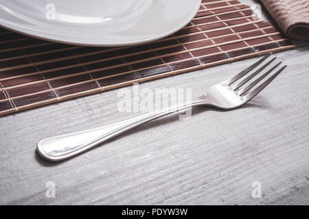 Edelstahl Gabel auf einen Tisch neben einem Teller auf Tischdecke - Vorbereitung Abendessen Konzept Stockfoto