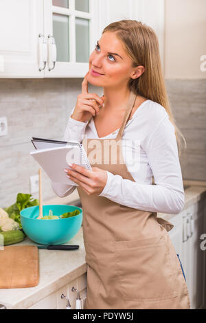 Schöne Frau Hobeln was zu kochen, während sie Kochbuch. Stockfoto