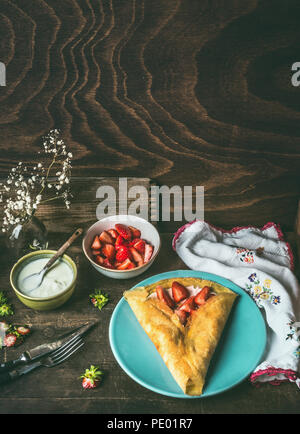 Hausgemachte Crepes auf dunklen rustikalen Küche Tisch mit Erdbeeren und Joghurt. Country Style food Still Life Stockfoto