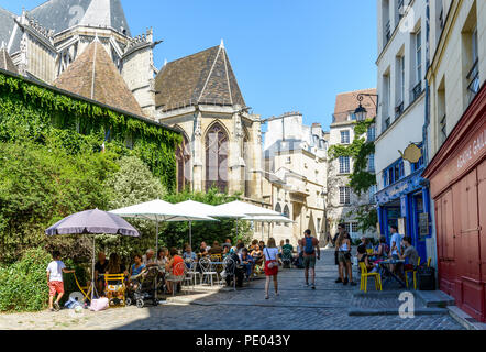 Ein Fußgänger gepflasterten Straße in Paris, Frankreich, hinter Saint-Gervais Kirche, mit Menschen, die das Mittagessen auf der Terrasse des Restaurant von einem sonnigen Tag. Stockfoto