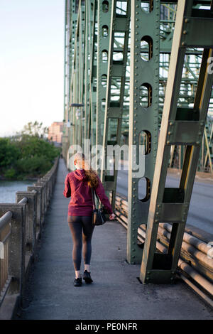 Mädchen mit langen Haaren und Tasche über die Schulter Spaziergänge durch die Columbia Interstate Hubbrücke mit Dreieck Traversen auf der anderen Seite der Ri angeschlossen Stockfoto