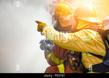 In der Nähe von zwei feuerwehrmänner Spritzwasser durch Hochdruckdüse Feuer umgeben von Rauch mit Flare und kopieren Raum Stockfoto