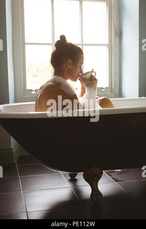 Frau bei einem Bad in der Badewanne, während einer Tasse Kaffee Stockfoto