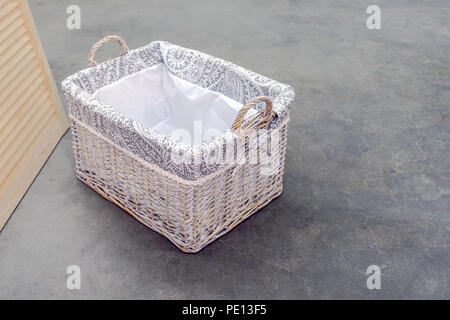 Wicker box von Rattan Boho Typ, mit Griffen steht auf einem grauen Betonboden. Stockfoto