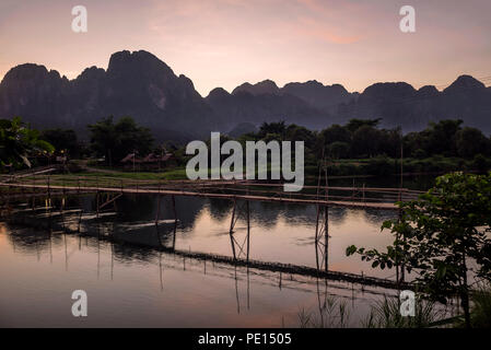 Herrlicher Sonnenuntergang über den Bergen dominieren Vang Vieng mit Blick auf den Fluss Nam Song und die hölzerne Brücke, Laos Stockfoto