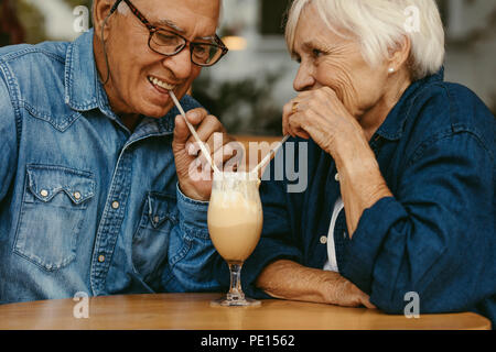 Nahaufnahme von Happy senior Paar in Liebe im Cafe trinken kalten Kaffee aus demselben Glas. Alte Mann und Frau genießen Sie einen kalten Kaffee auf Tisch. Stockfoto