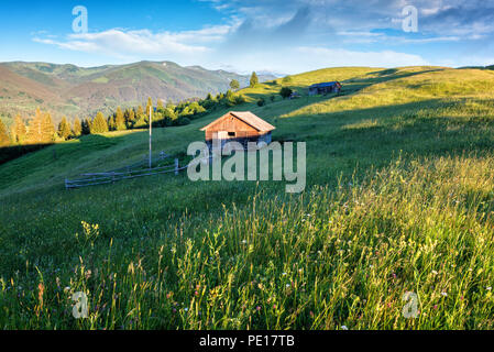 Sonnigen Bergwiese mit hölzernen Gebäude, grünes Gras, blauen bewölkten Himmel und Berge, Natur Sommer Landschaft Stockfoto