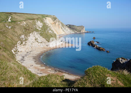 Mit Blick auf eine Bucht des South West Coast Path in der Nähe von Durdle Door mit klarem, blauem Wasser, Sandstrand und einem klaren blauen Himmel Stockfoto