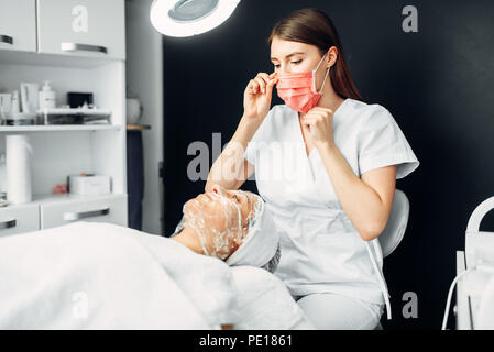 Kosmetikerin Uhren auf Patienten in der Maske, Beseitigen von Falten, kosmetologie Klinik. Gesichtspflege, Verjüngung Verfahren in Spa Salon, Gesundheit Stockfoto