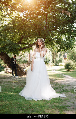 Junge Mädchen in einem weißen Kleid auf der Wiese. Frau in einem schönen langen Kleid in den Garten stellen. Herrliche Braut ein Hochzeitskleid. Stockfoto