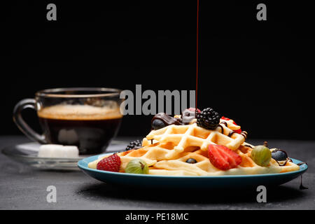 Foto Tasse schwarzen Kaffee mit Zucker mit Wiener Waffeln mit Erdbeeren, Himbeeren, Stachelbeeren und Schokolade Stockfoto