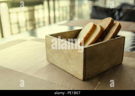 In Holz geschnitten Brot Brot Box. Vier Stücke Brot in einem schönen breadbox auf einem Tisch in einem Café. Frisches Brot in Holz- Brot Box mit Hintergrund Stockfoto