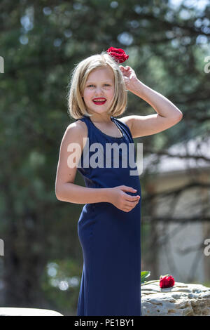 Hübsche, junge blonde Frau. preteenn, Mode schießen. Standing Rock, mit einer roten Rose in der Hand. 3/4 Profil, blaues Kleid, Model Released. Stockfoto