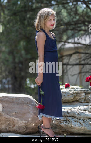 Hübsche, junge blonde Frau. preteenn, Mode schießen. Standing Rock, mit einer roten Rose in der Hand. 3/4 Profil, blaues Kleid, Model Released. Stockfoto