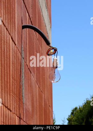 Einzelne Glühbirne hängen von einem Kabel auf der Außenseite eines neu errichteten Wand an einem Haus in Murviel-lès-Béziers, Frankreich Stockfoto