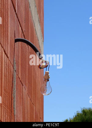 Einzelne Glühbirne hängen von einem Kabel auf der Außenseite eines neu errichteten Wand an einem Haus in Murviel-lès-Béziers, Frankreich Stockfoto