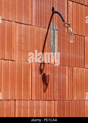 Einzelne Glühbirne hängen von einem Kabel auf der Außenseite eines neu errichteten Wand an einem Haus in Murviel-lès-Béziers, Frankreich Stockfoto