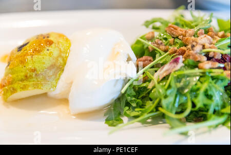 Klassische Salat mit Birne, Rucola oder rauke Blätter, gehobeltem Parmesan und Walnüsse. Beträufelt mit Olivenöl, Zitrone Essig, Burrata, gewürzt, macadamia. Stockfoto